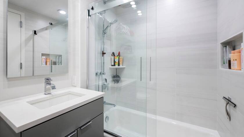 Remodeled bathroom with a glass shower and tub enclosure, gray vanity and white counter