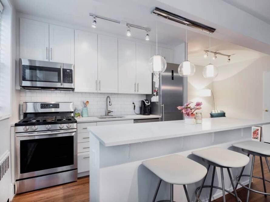 Remodeled white kitchen with quartz counters, stainless steel appliances and an island with stools