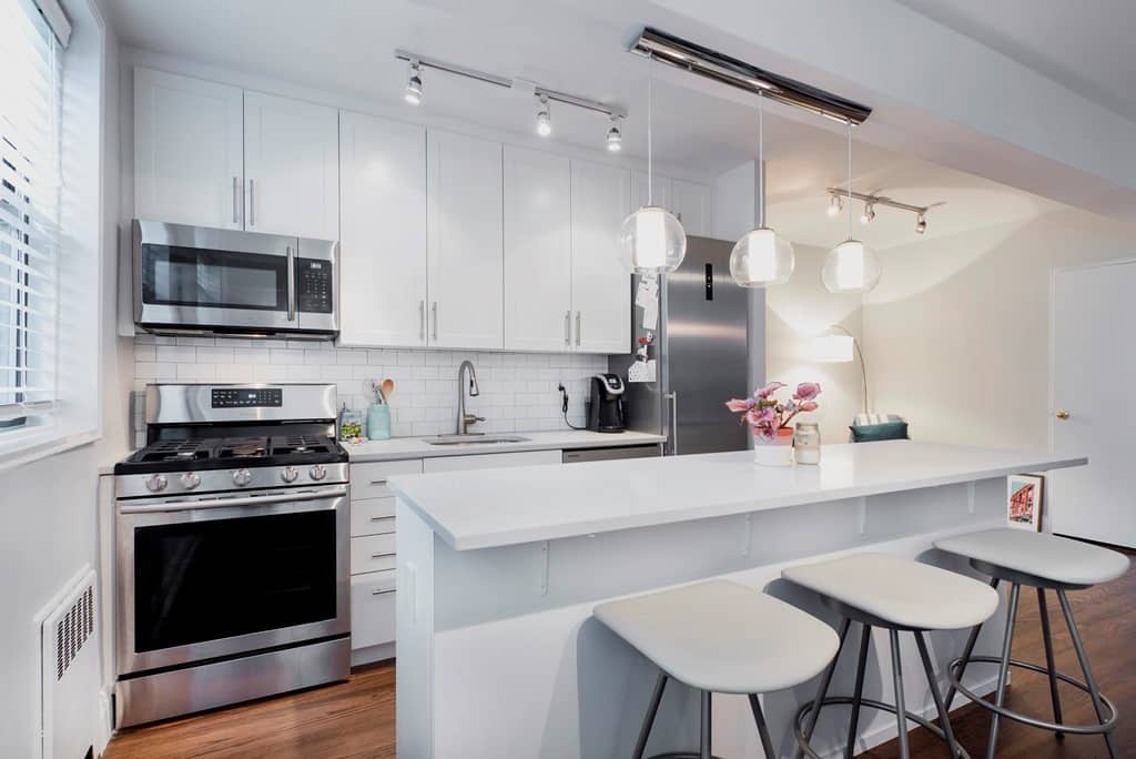 Remodeled white kitchen with quartz counters, stainless steel appliances and an island with stools