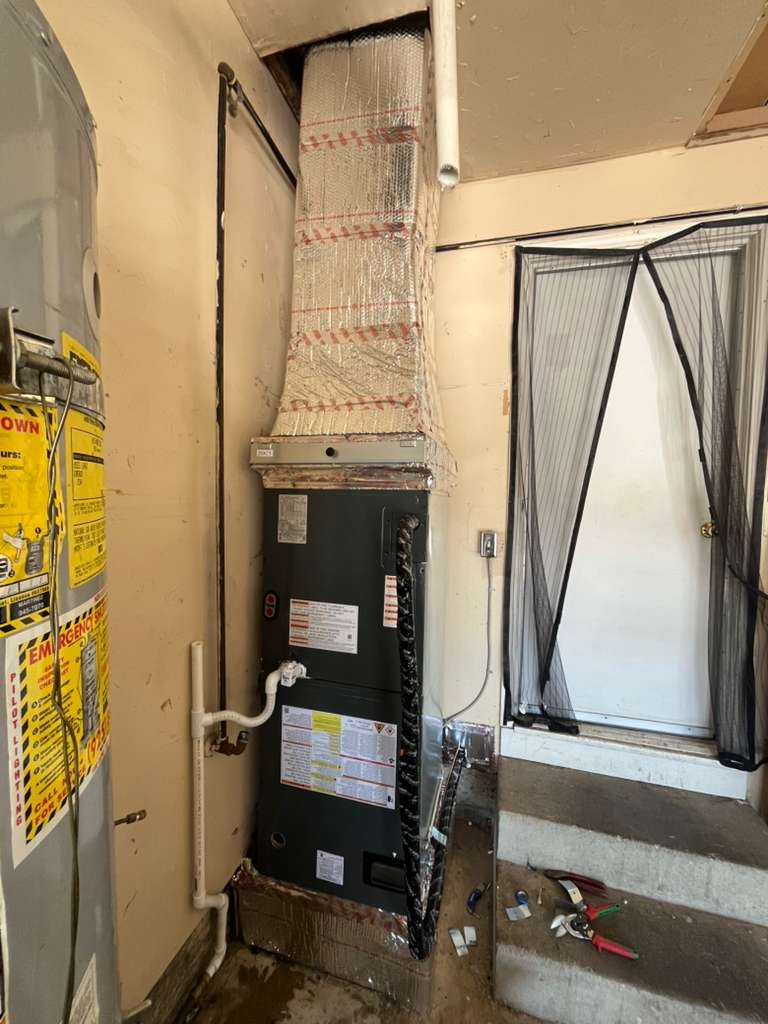 Close view of the new dark grey air handler in the Antioch garage, with its refrigerant and condensate lines