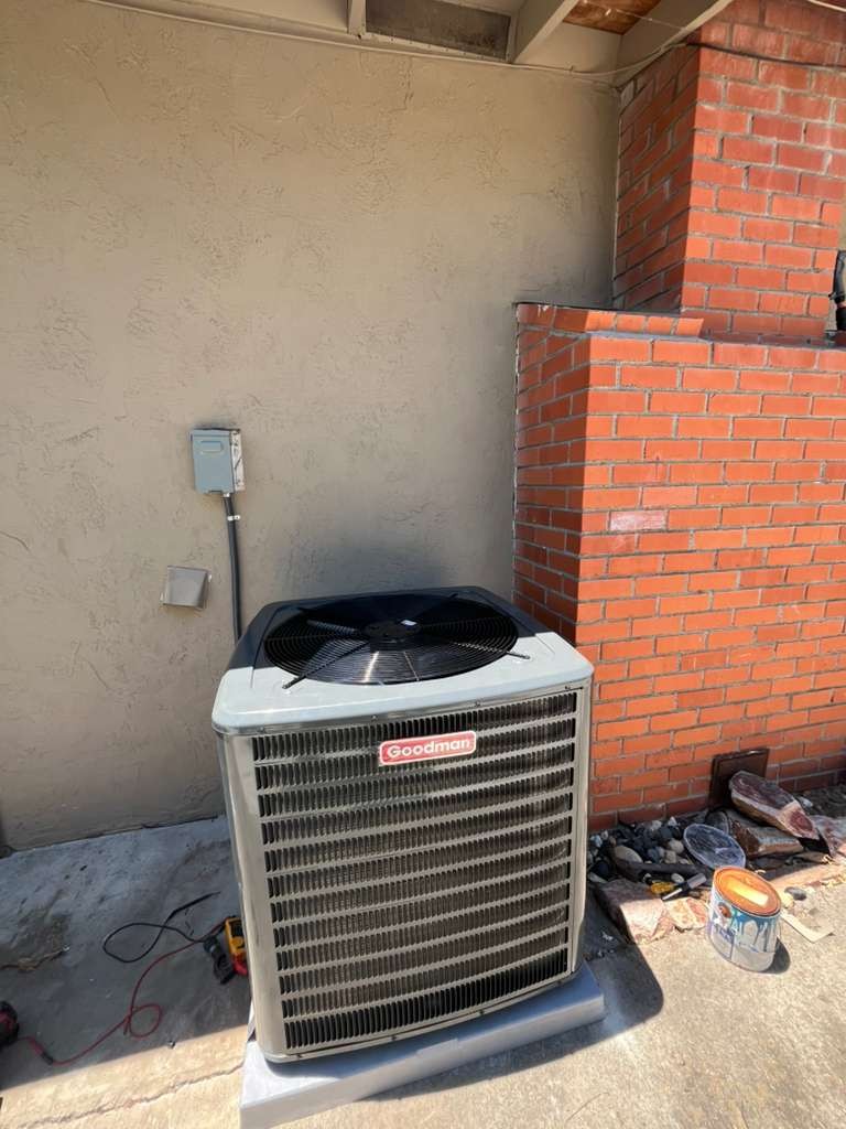 The new Goodman heat pump unit on its pad beside the Antioch house, with the disconnect box on the wall above