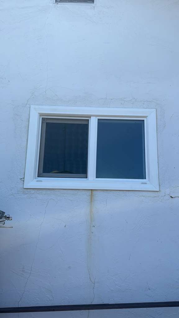 A new white vinyl sliding window set into the stucco wall of the Campbell house