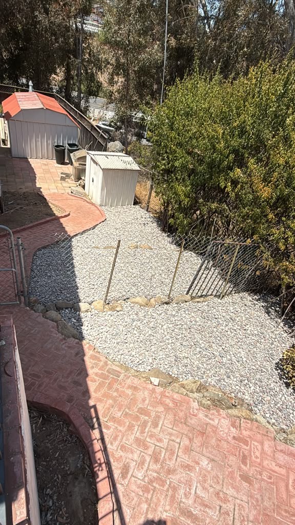 Crushed gravel covering a side yard between brick paving and a chain-link fence in El Cajon