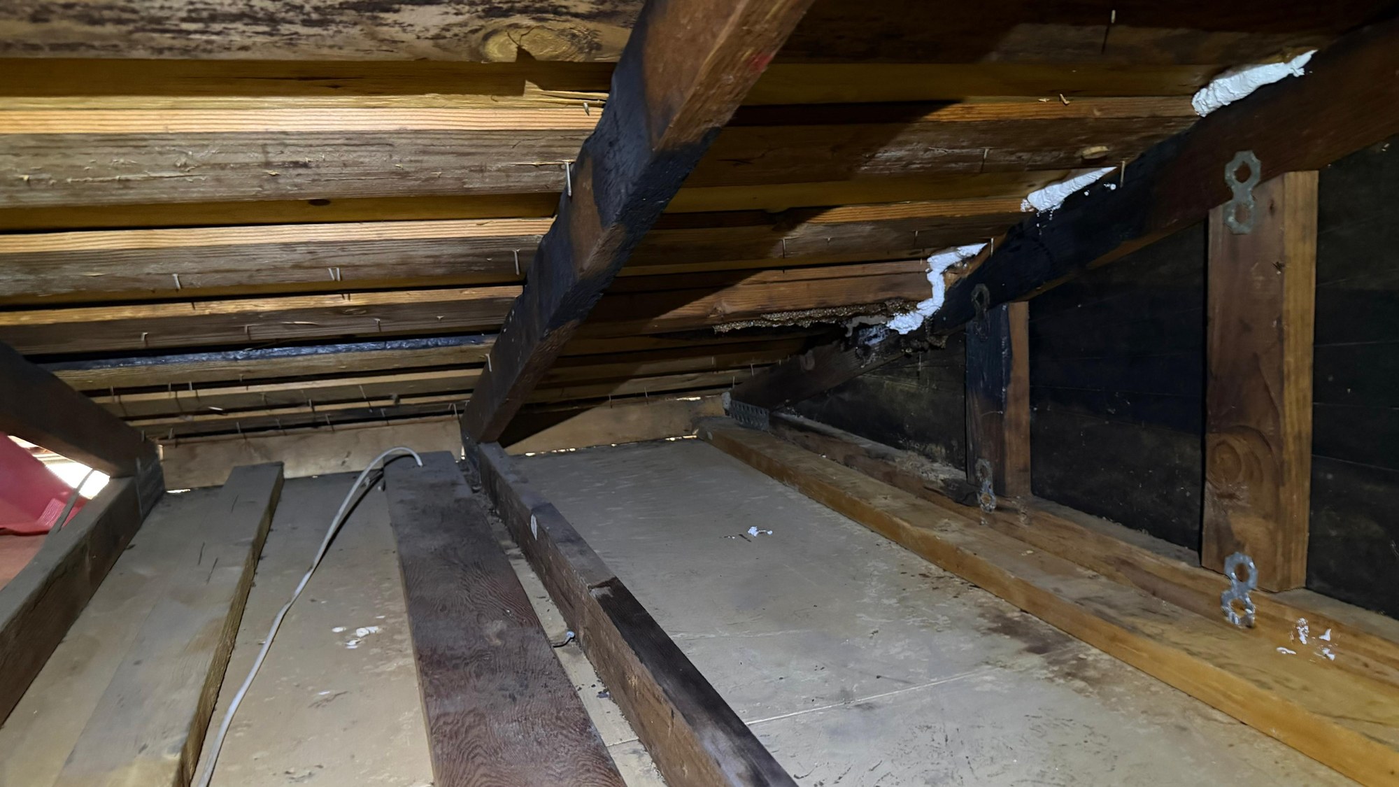 Bare attic floor with white foam sealant along the top plate and rafters