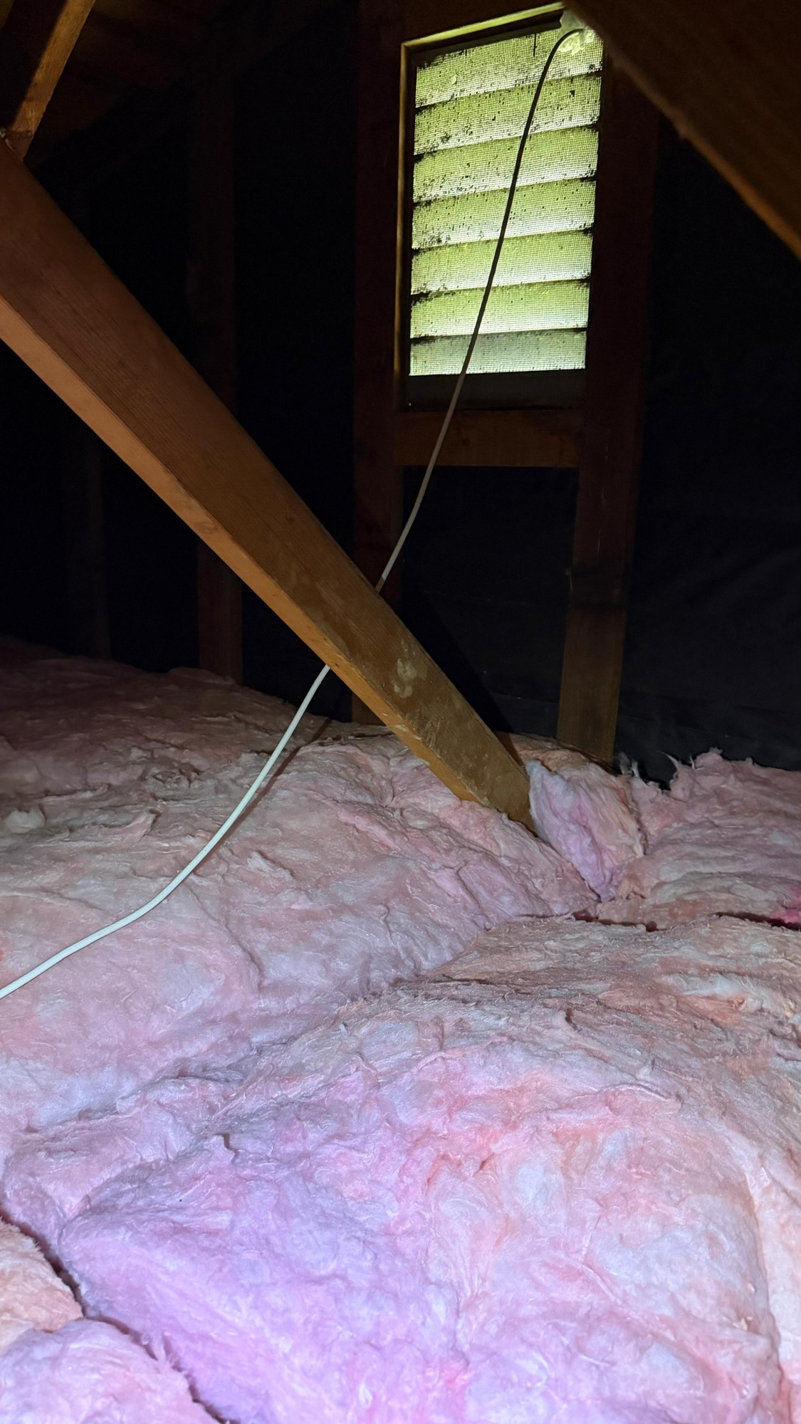 New pink batts laid below a gable vent in the attic