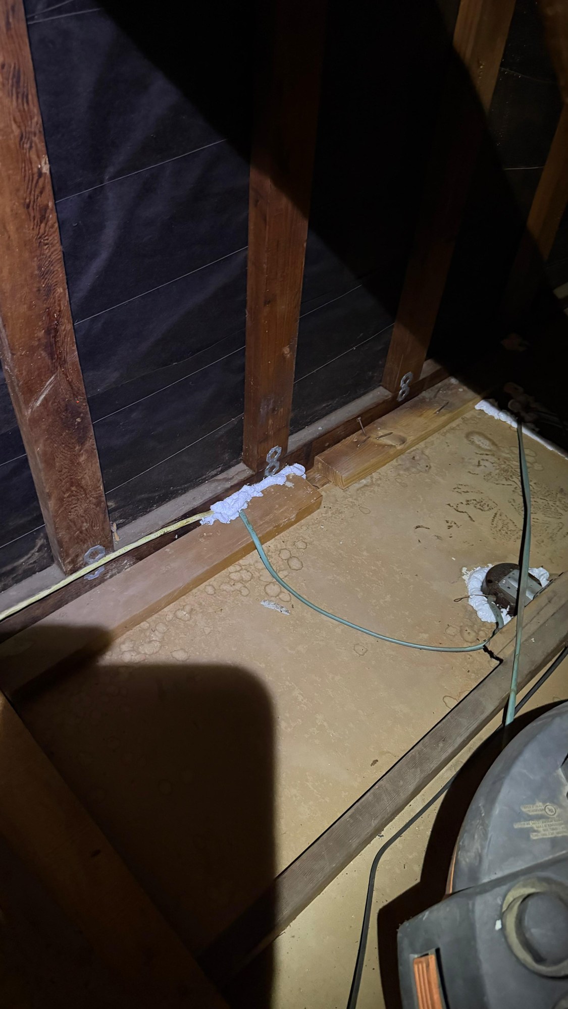 Cleared attic floor at a wall, with sealant at the plate and a removal vacuum in the corner