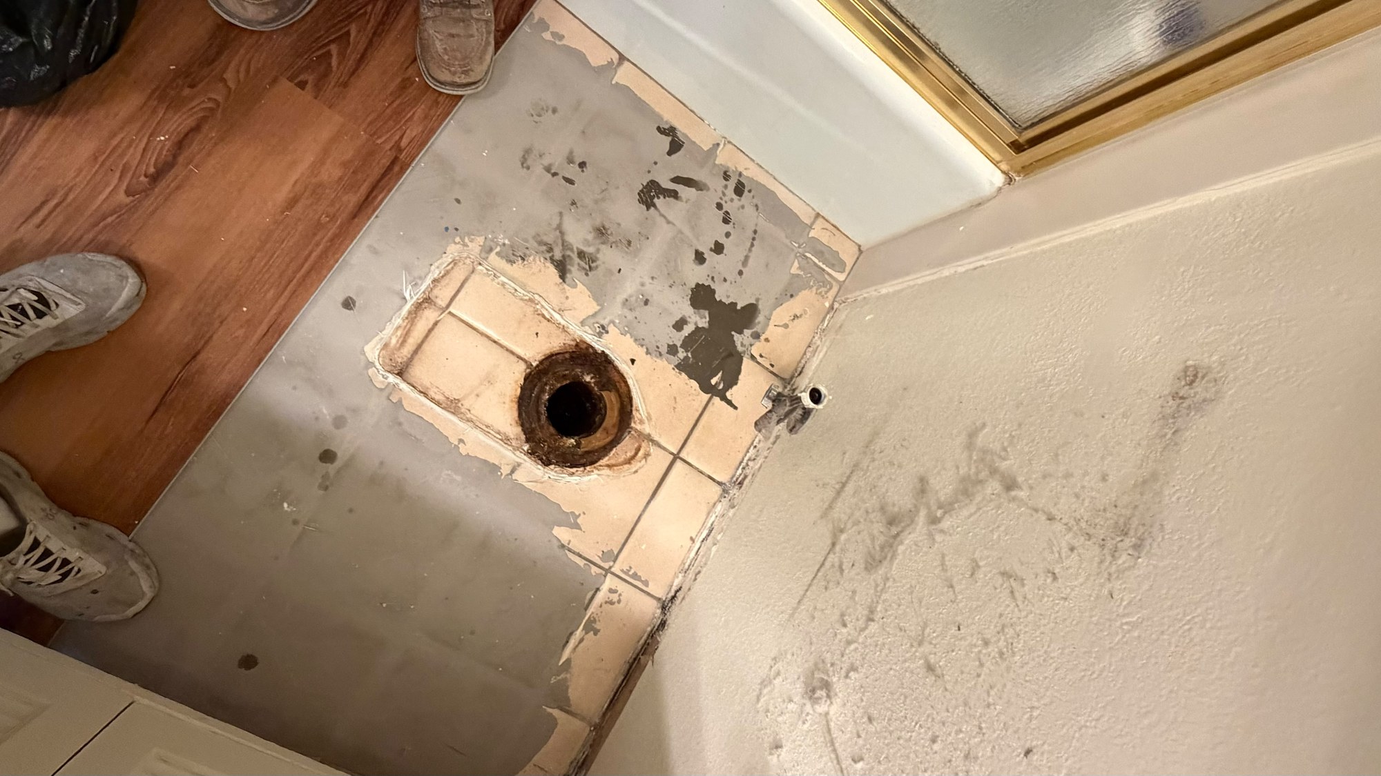 Bathroom floor with the toilet removed, grey patching over the tile joints and new plank flooring at the doorway