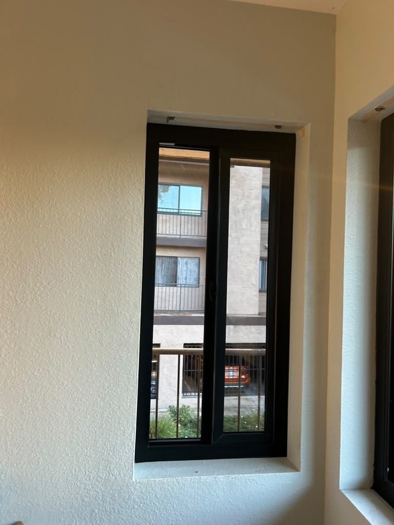 A new black vinyl sliding window set into a plain textured wall in the San Diego home