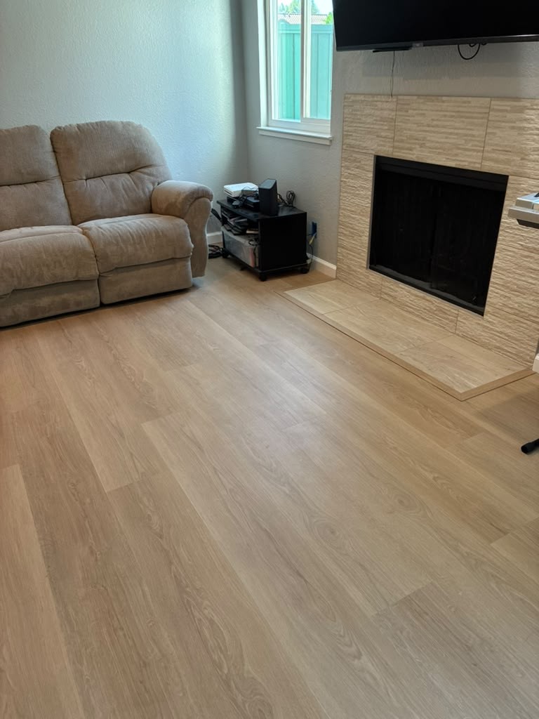 Light oak-look luxury vinyl plank floor running up to a tiled fireplace hearth in the San Jose living room