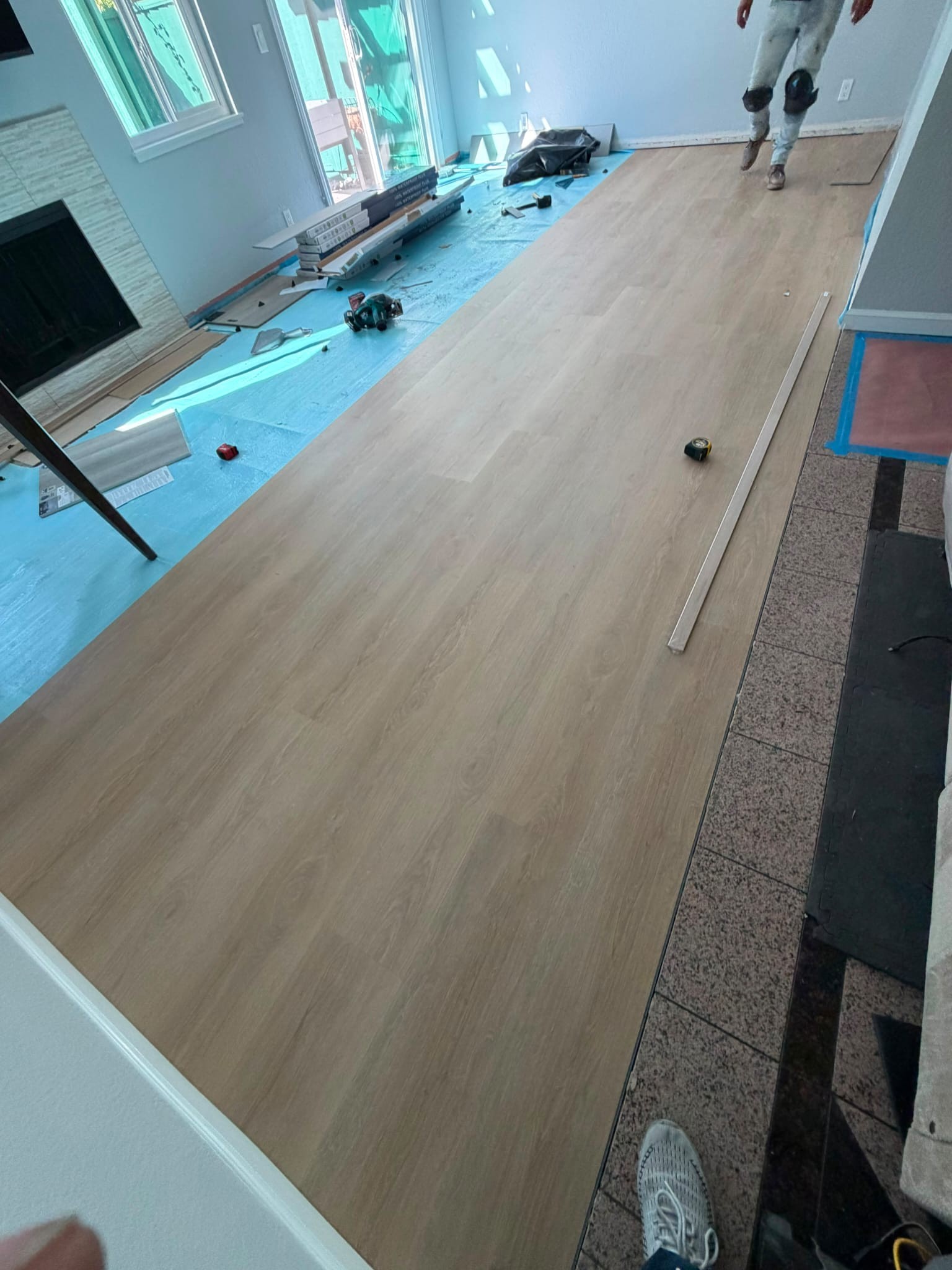 A long run of new vinyl planks beside the tiled entry, with a trim strip lying on the floor