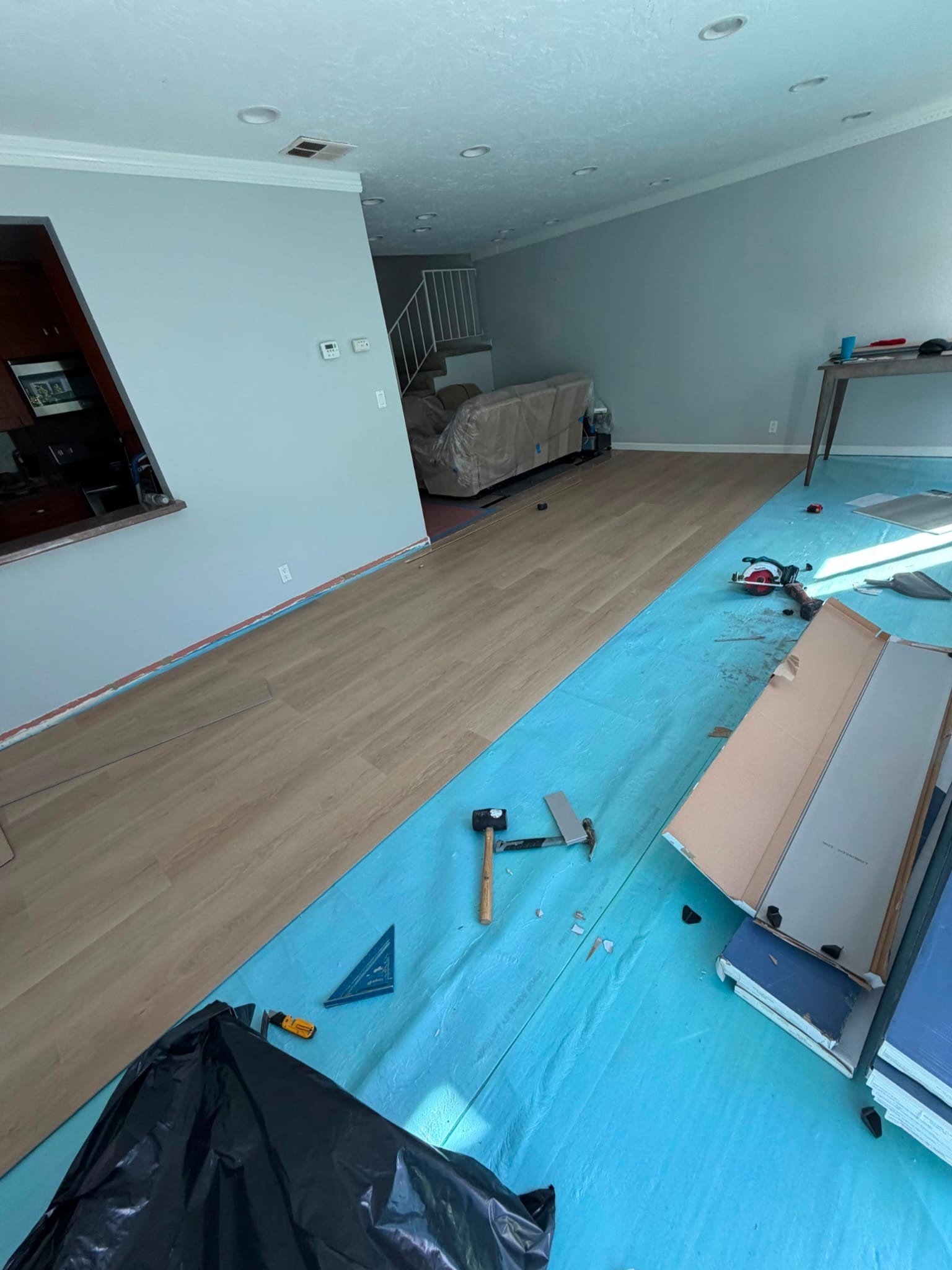 New light oak-look planks laid over the far end of the room, with tools and plank cartons in the foreground