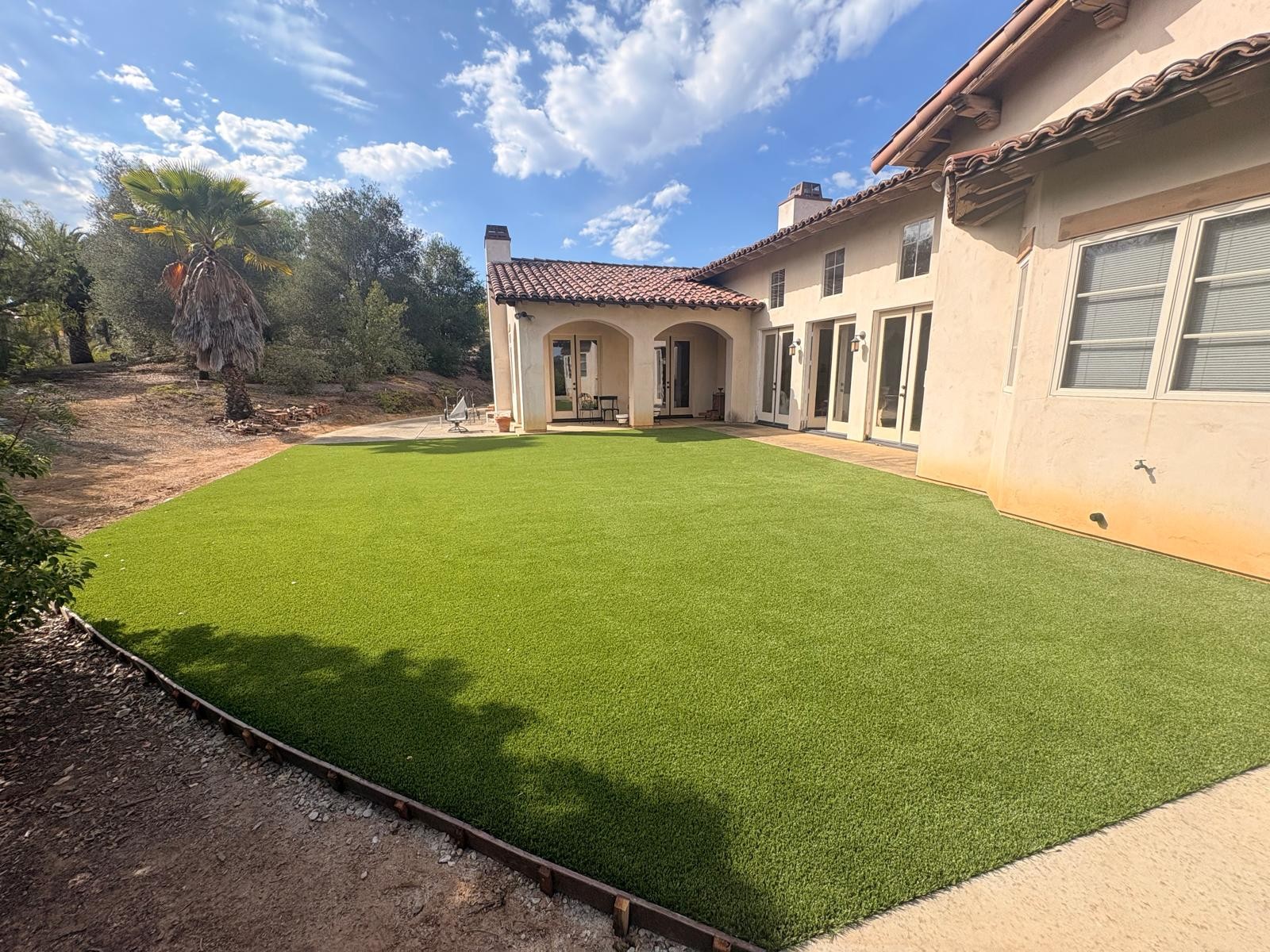Green artificial turf lawn wrapping the back of a stucco house with a tile roof in Valley Center