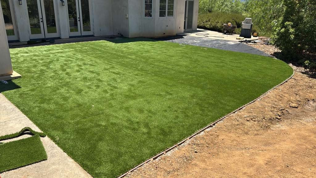 Newly laid artificial turf with a curved bender-board edge beside a dirt bed, offcuts on the path